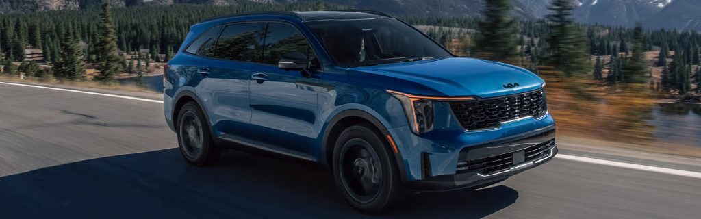 A sleek blue Kia SUV driving on a scenic road surrounded by mountains