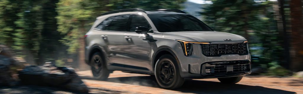 A silver Kia Sorento driving off-road through a forested area.