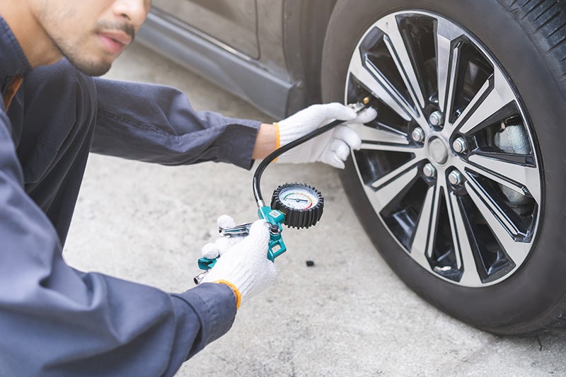 A person in gloves is using a tire pressure gauge to check the pressure of a car tire.
